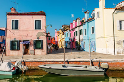 Boats moored on canal by buildings in city against sky