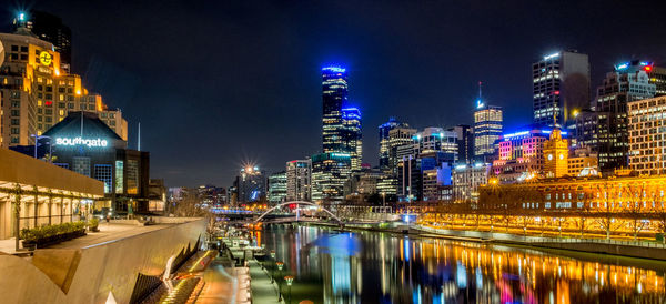 Illuminated buildings by river against sky in city at night