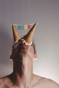 Close-up of shirtless man with ice cream cones on eyes against wall