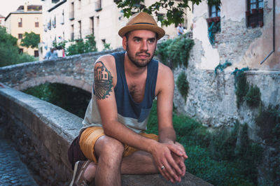 Man with hat sitting on retaining wall in town