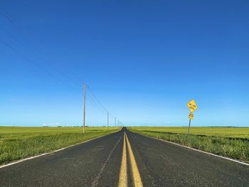 Road amidst field against clear blue sky