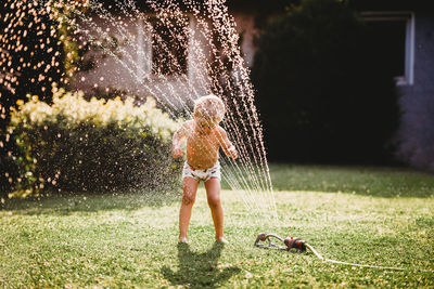 Young boy playing with water from the sprinkler in the garden