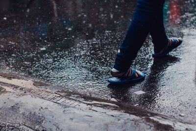 Low section of man walking on road during rain