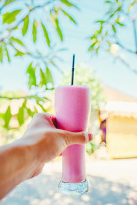 Cropped hand of woman holding smoothie against sky