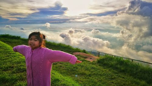 Portrait of girl standing on field against cloudy sky