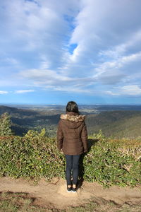 Rear view of woman standing on mountain against cloudy sky