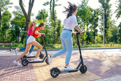 Full length of women riding push scooter on the street