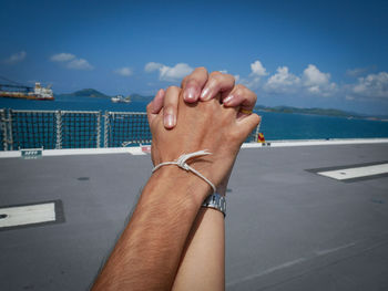 Cropped image of couple holding hands against sea on road