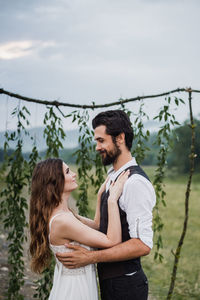 Side view of bride and bridegroom standing on field