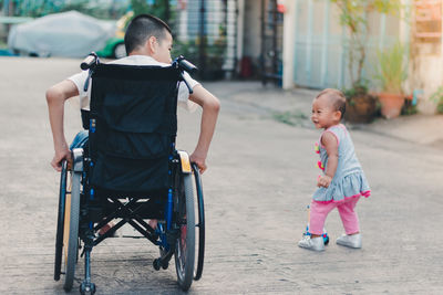 Rear view of brother on wheelchair with sister outdoors