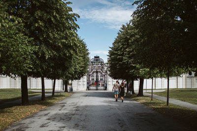 People on walkway amidst trees and buildings against sky