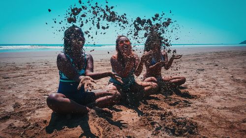 Young friends playing with sands while sitting at beach