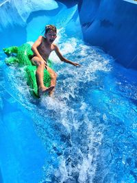 Playful boy sliding on water slide during sunny day