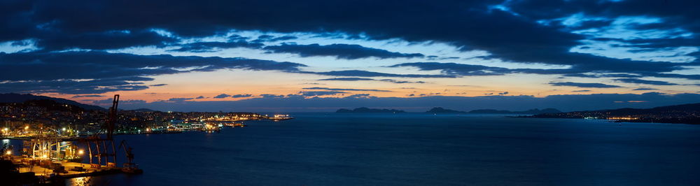 Sea by illuminated buildings against sky at sunset