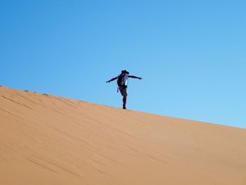 Low angle view of man standing on desert against clear blue sky