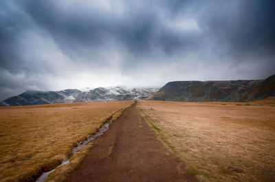 Dirt road leading towards mountains against sky