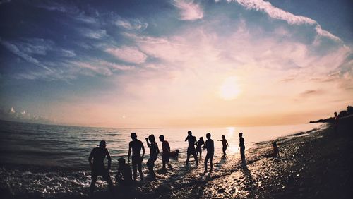 Silhouette people at beach against sky during sunset