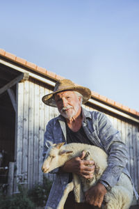 Smiling farmer carrying sheep at farm