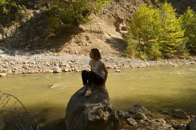 Young woman sitting on rock at riverbank