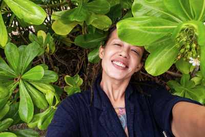 Funny smiling woman taking selfies among tropical leaves.