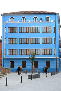 People walking on building against clear blue sky