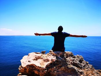 Rear view of man with arms outstretched looking at sea against sky