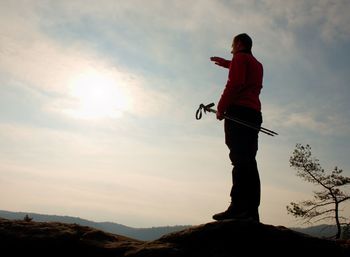 Tourist in windcheater with sporty tracking poles in hands on rocky view point. spring sunny day.