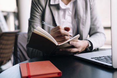Young businesswoman writing in diary with pen at table in cafe