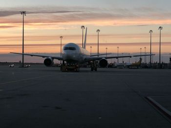 Airplane on airport runway against sky during sunset