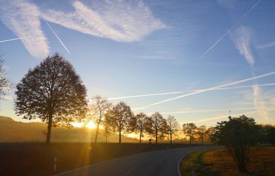 Road by trees against sky during sunset