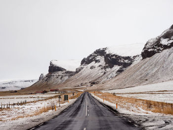 Road amidst snowcapped mountains against clear sky