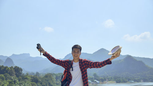 Man with arms outstretched standing on mountain range against sky