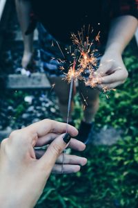 Close-up of friends holding sparkler at railroad track