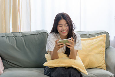 Young woman using phone while lying on sofa at home