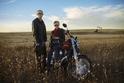 Portrait of man standing while woman sitting on bike against sky