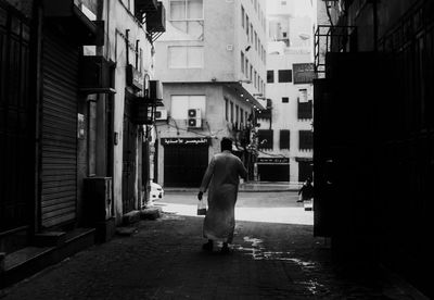 Rear view of a man walking along buildings