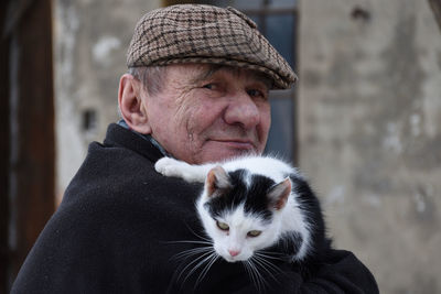 Portrait of senior man carrying cat against house