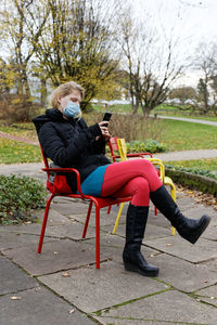 Full length of woman using mobile phone while sitting on chair