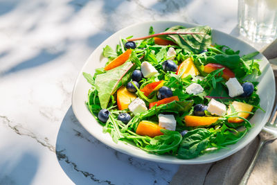 Salad with nectarines, blueberries, arugula, spinach and feta cheese on white marble background 