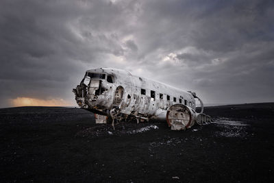 Abandoned airplane at beach against cloudy sky