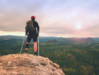 Man hiker wearing supportive leg brace and against the crutches. natural forest park in background