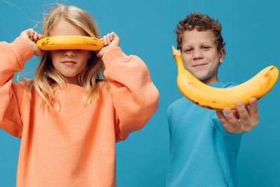 Siblings playing with banana against blue background