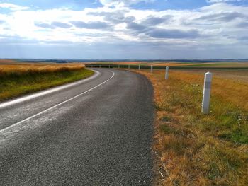 Empty road amidst field against sky