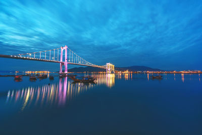 Illuminated bridge over sea against sky at dusk