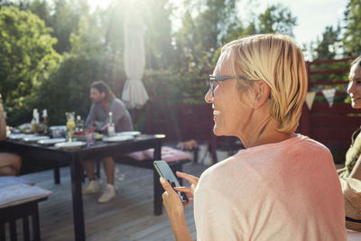 Rear view of happy woman with mobile phone in back yard on sunny day