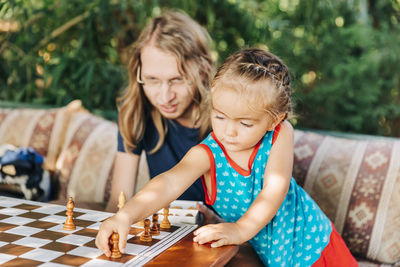 Father teaching chess to daughter while sitting on sofa at home