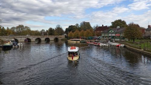 Boats in river by buildings against sky