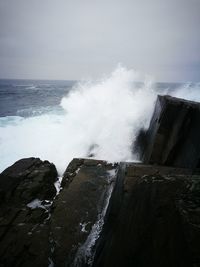 Waves breaking on rocks against sky