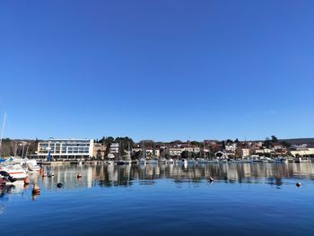 Buildings by river against clear blue sky