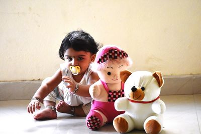 Cute girl sitting with stuffed toys against wall